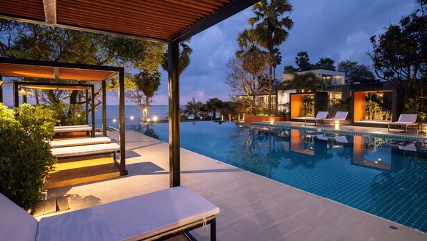 An infinity pool with lounge chairs and a pergola, surrounded by palm trees and a modern building. - Sunshine Paradise Resort (Thap Sakae)