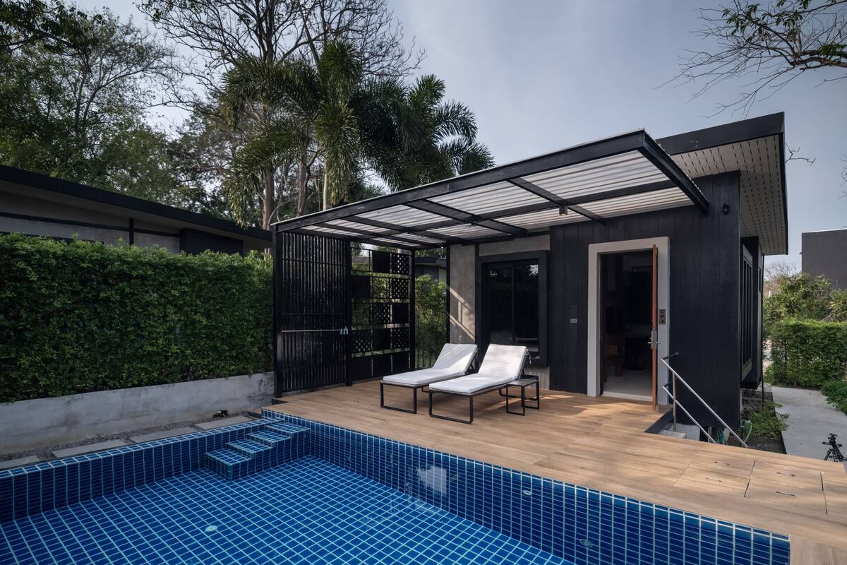 A modern outdoor pool area with two lounge chairs and a covered seating area.