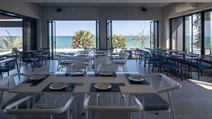 A modern dining area with tables and chairs, large windows offering a view of the ocean and palm trees. - Sunshine Paradise Resort (Thap Sakae)