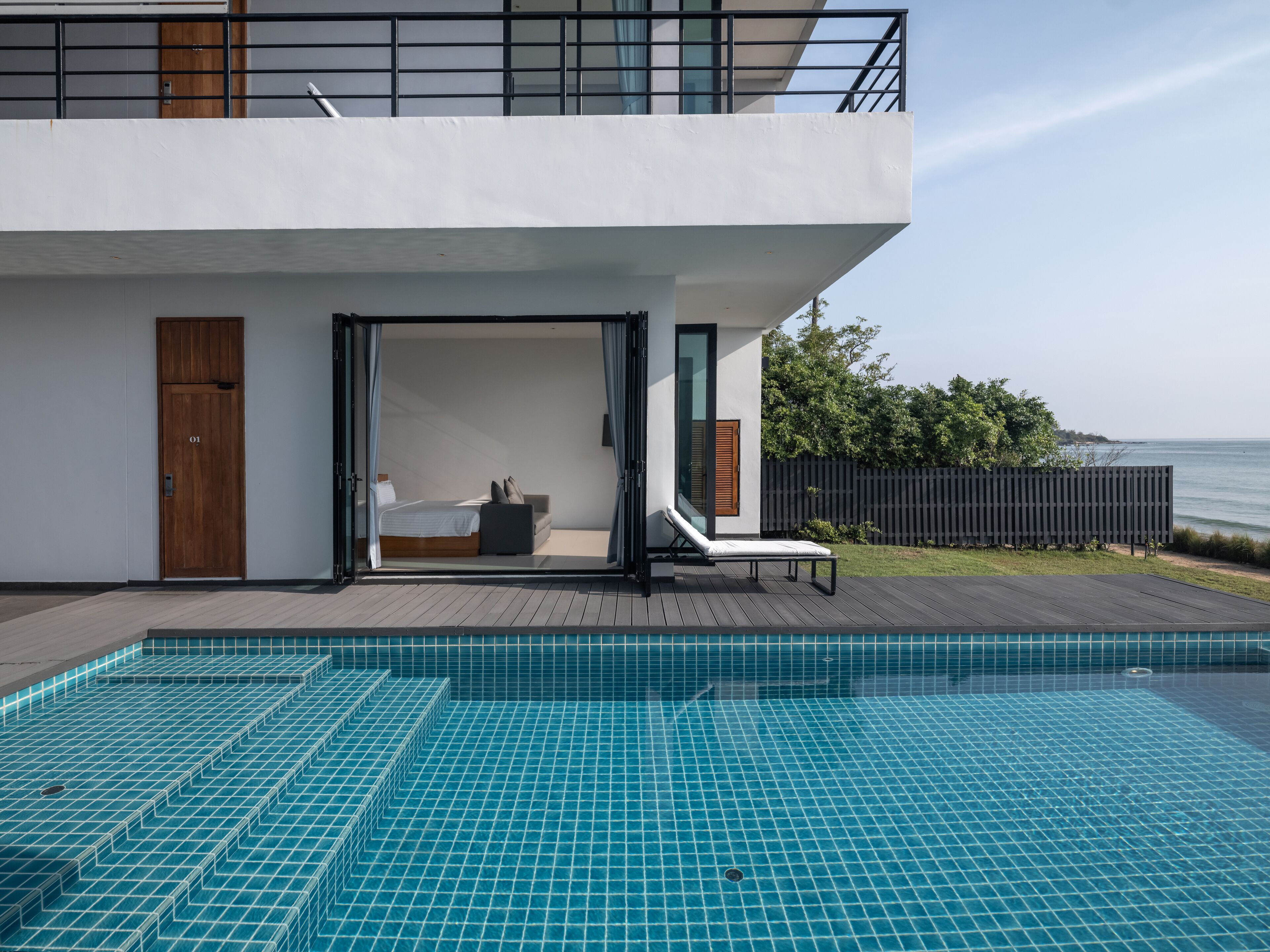 A modern house with a pool, a bedroom with a bed and a chair, and a view of the sea.