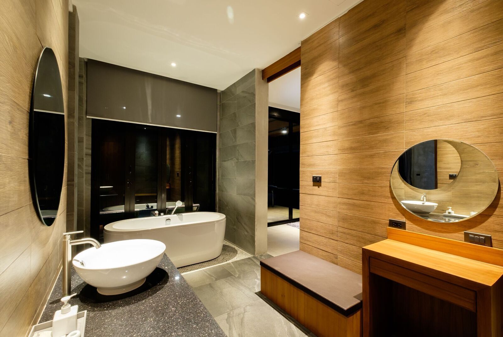 A modern bathroom with a freestanding bathtub, a round mirror, and a wooden vanity.