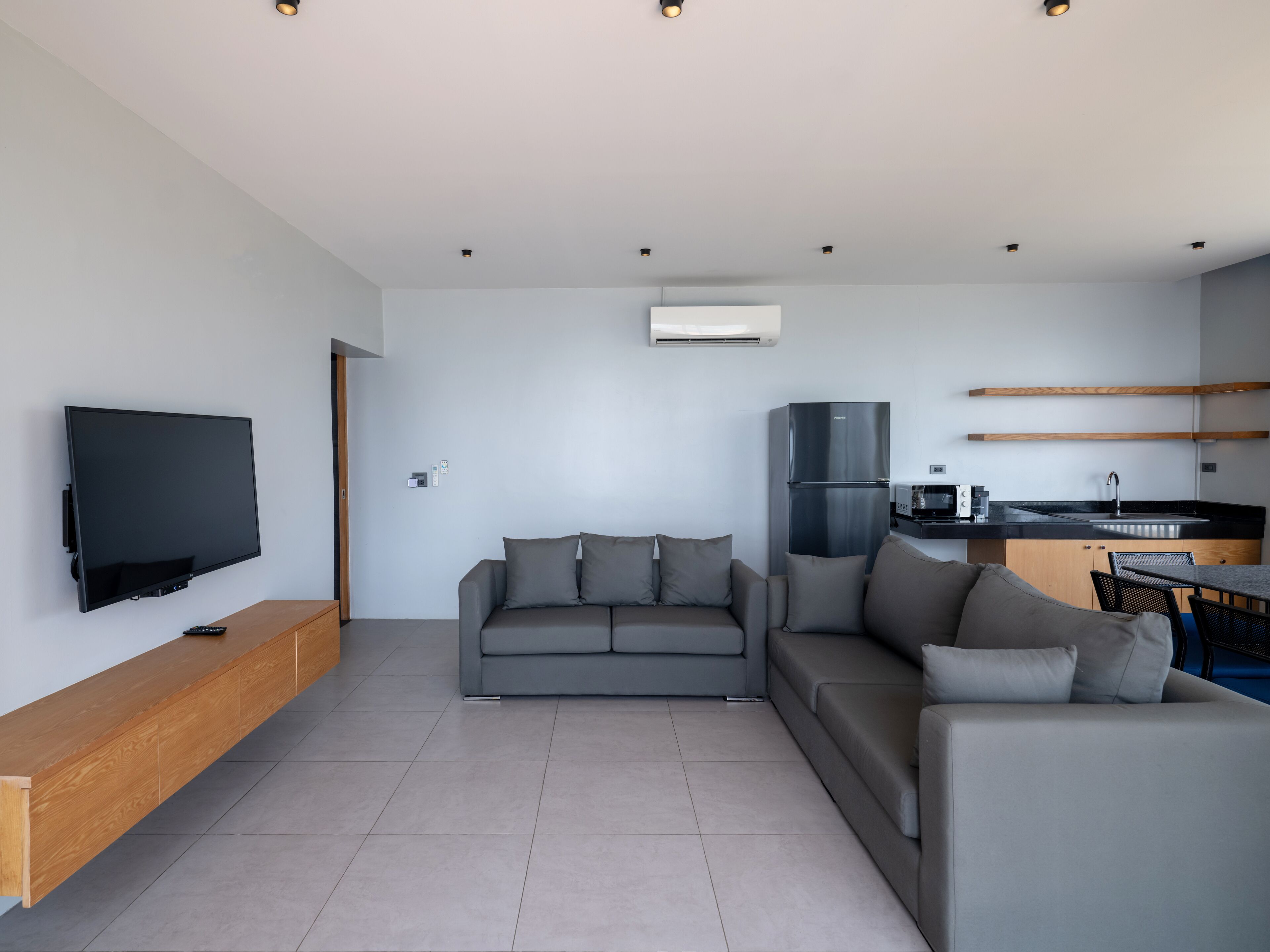 A modern living room with a flat-screen TV, a grey sofa, and a wooden bench.