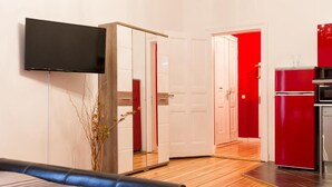Una habitación moderna con cama, televisor, espejo, refrigerador rojo y piso de madera.