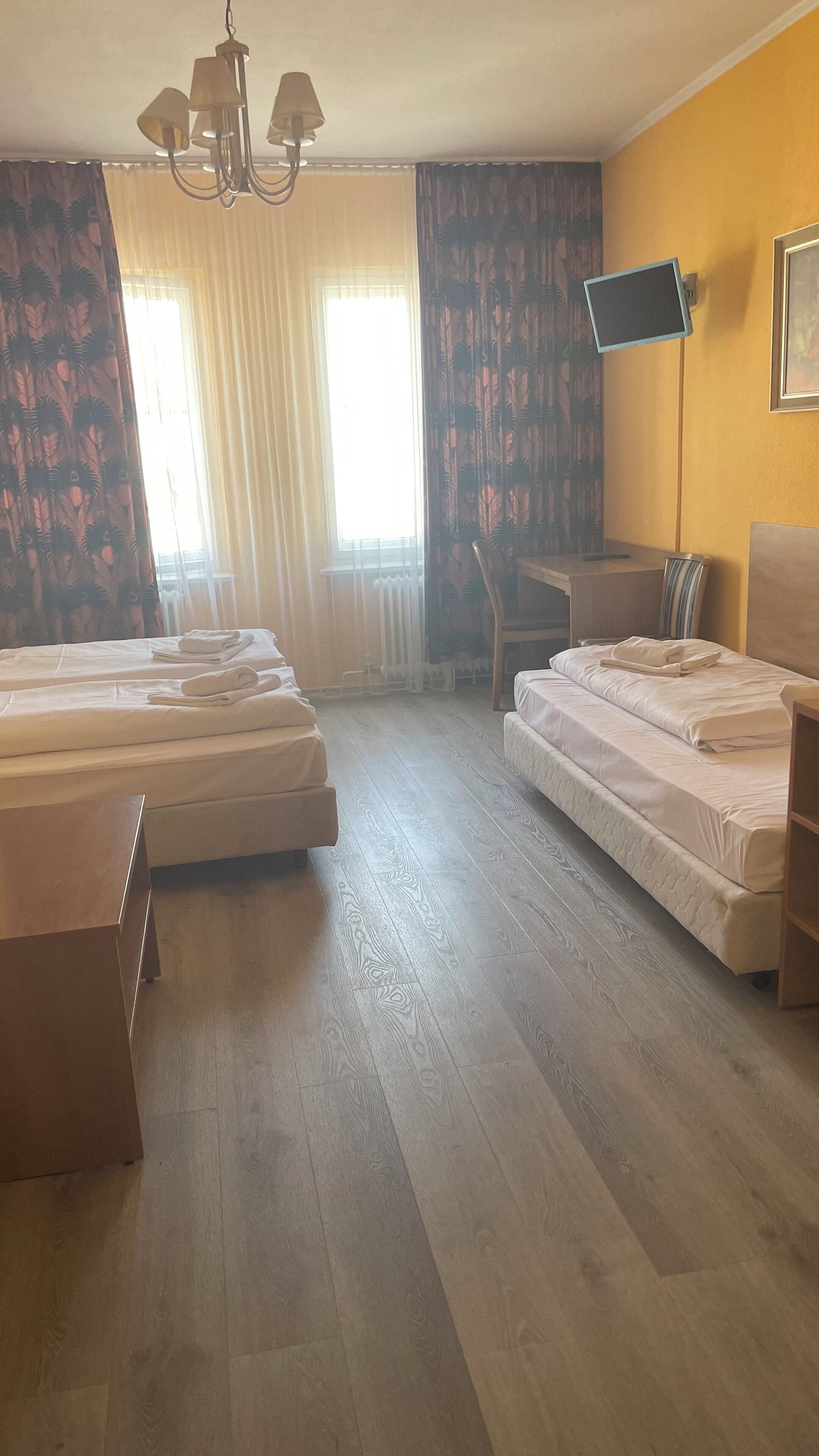 A hotel room with two beds, a desk, a chair, a TV, and a chandelier.