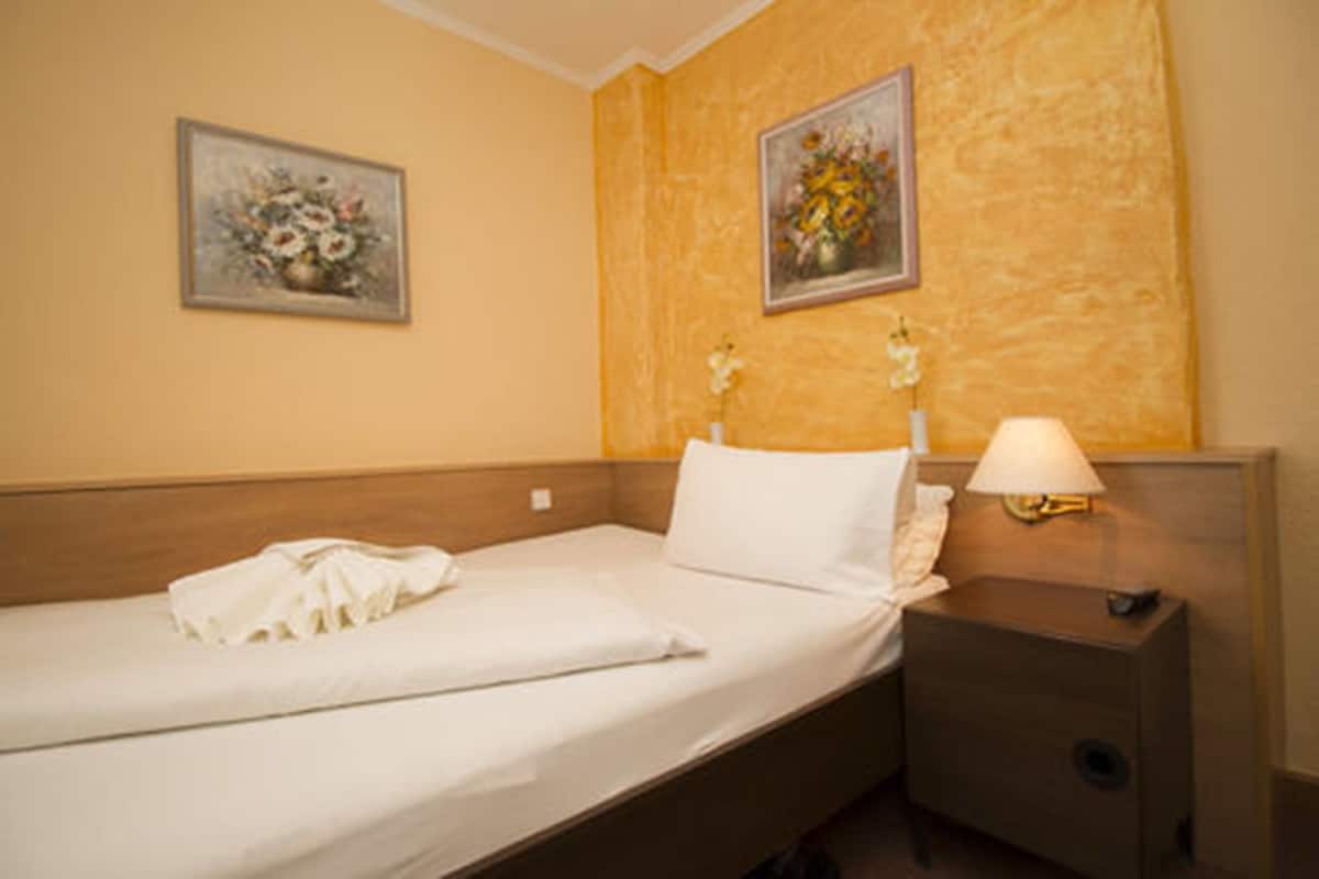 A neatly made bed with white linens, a bedside lamp, and two floral paintings on the wall.