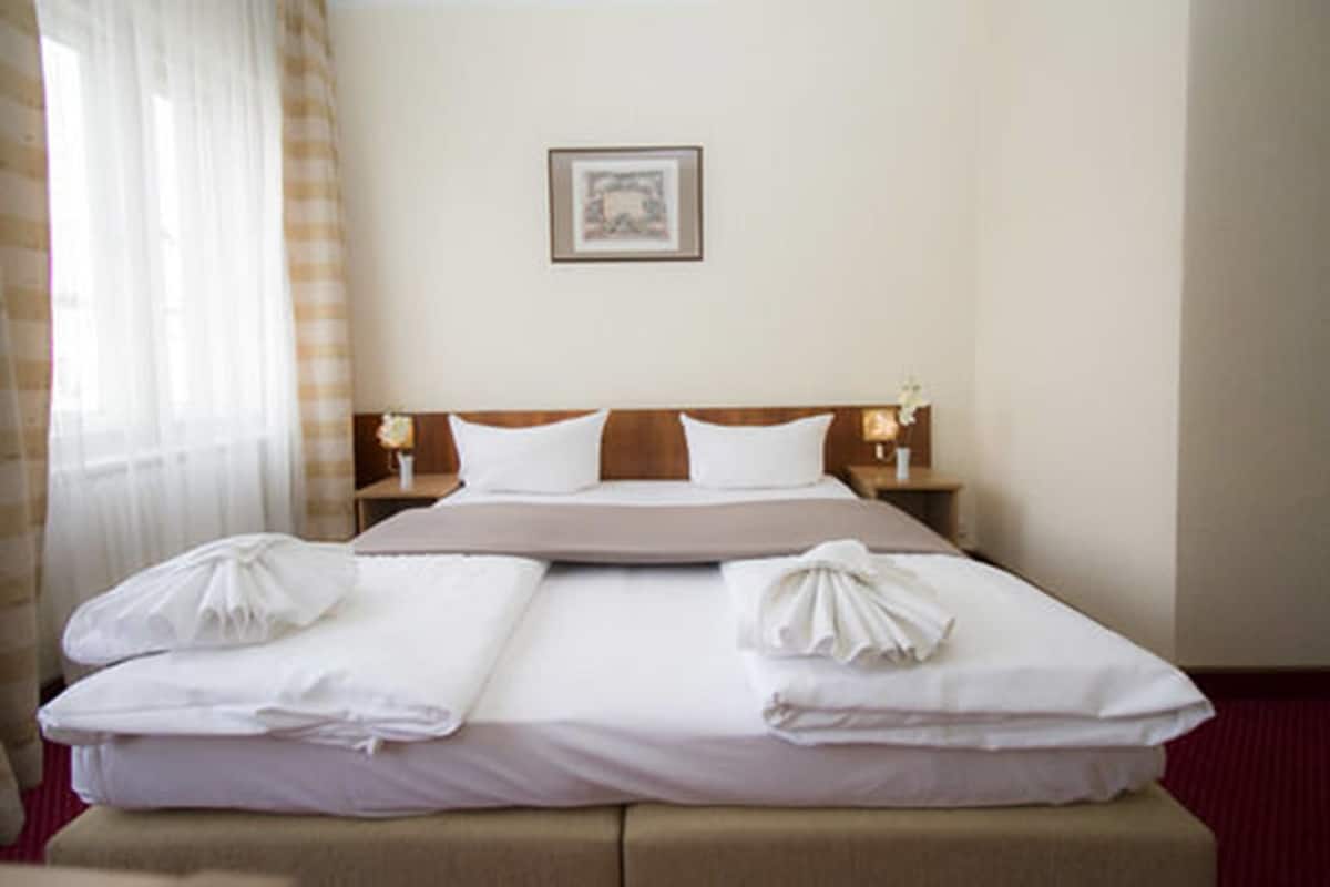 A hotel room with a large bed, two bedside tables, a framed picture on the wall, and a window with curtains.