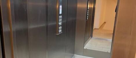 Un ascensor moderno con panel de control, paredes metálicas y suelo de baldosas.