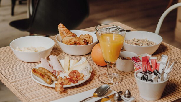 A breakfast table with croissants, orange juice, cereal, and condiments.