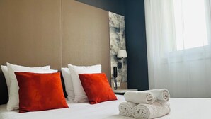 A hotel room with a large bed, two red pillows, a white bedspread, and a rolled white towel on the side.