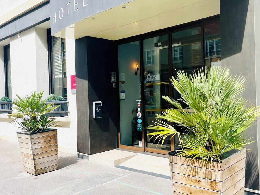 Exterior del hotel 'BRISTOL HOTEL', con fachada moderna, un amplio acceso de vidrio y dos plantas en macetas al frente.