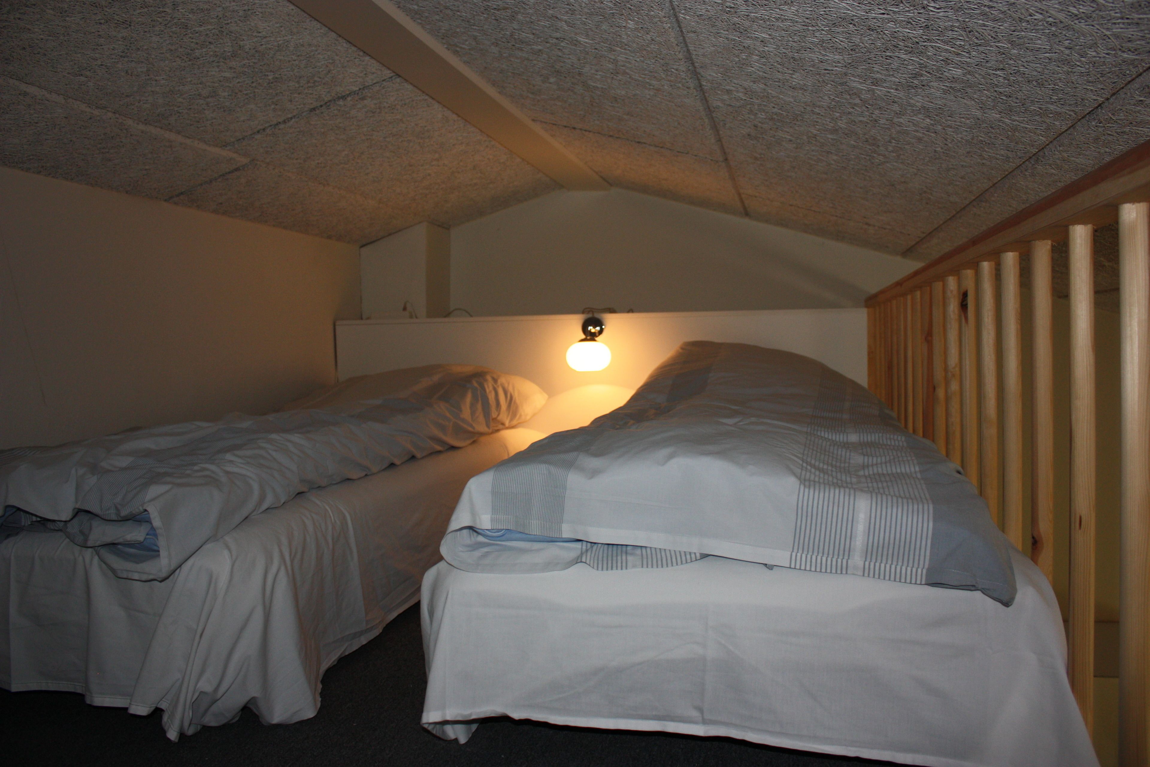 A small, dimly lit room with two single beds, a wooden headboard, and a ceiling light.