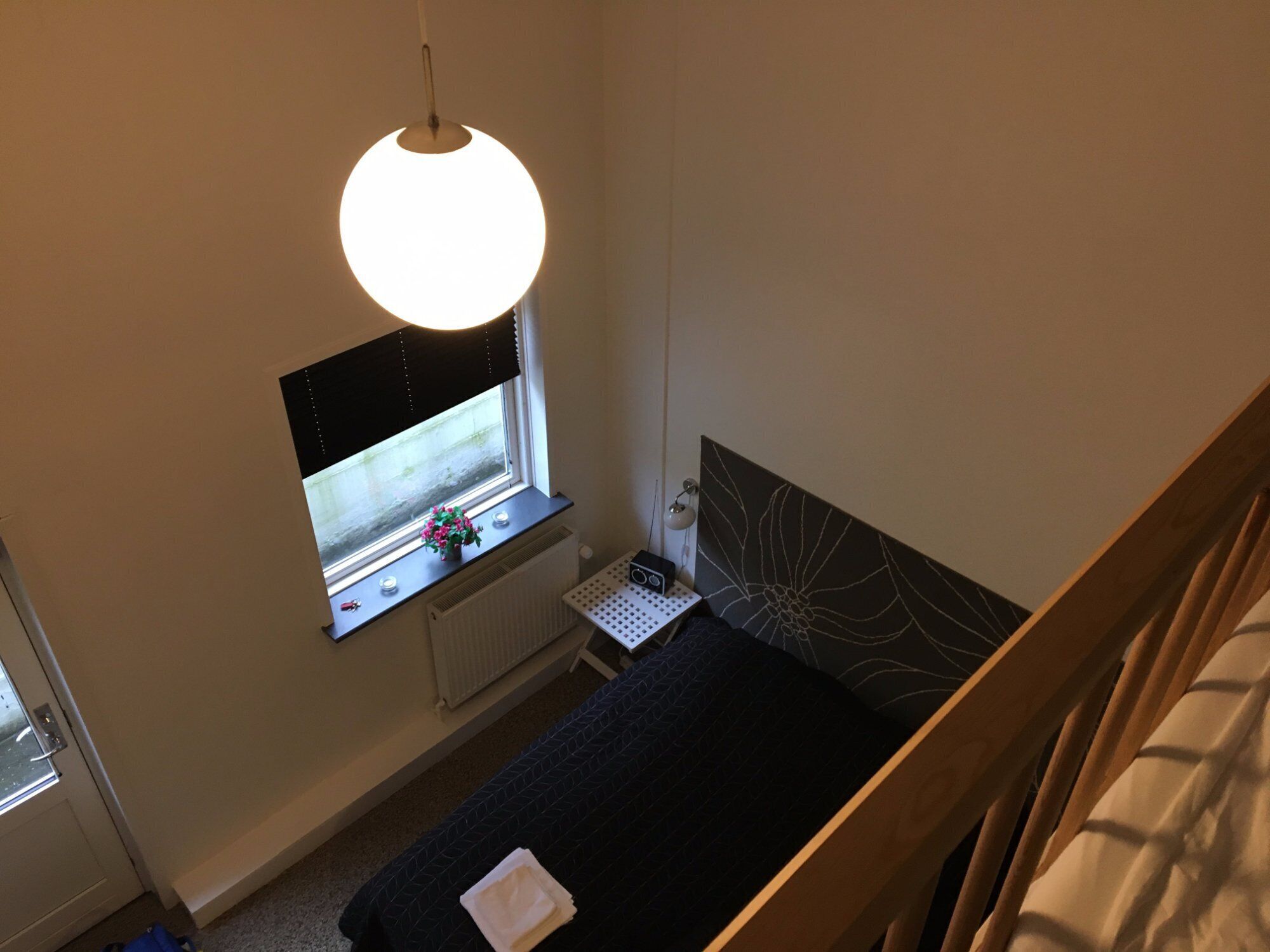 Ein Schlafzimmer mit Bett, einem Fenster mit Blick, einem Schreibtisch mit Lampe und einem Wandradiator.