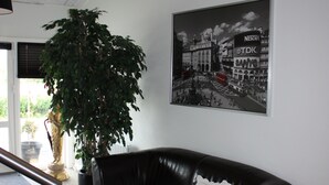 Una sala de estar moderna con un sofá de cuero negro, una planta grande en maceta, una lámpara negra y un cartel en blanco y negro de un paisaje urbano en la pared.