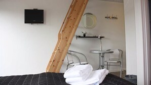 Un dormitorio con cama, televisión, espejo, una mesita y una silla.