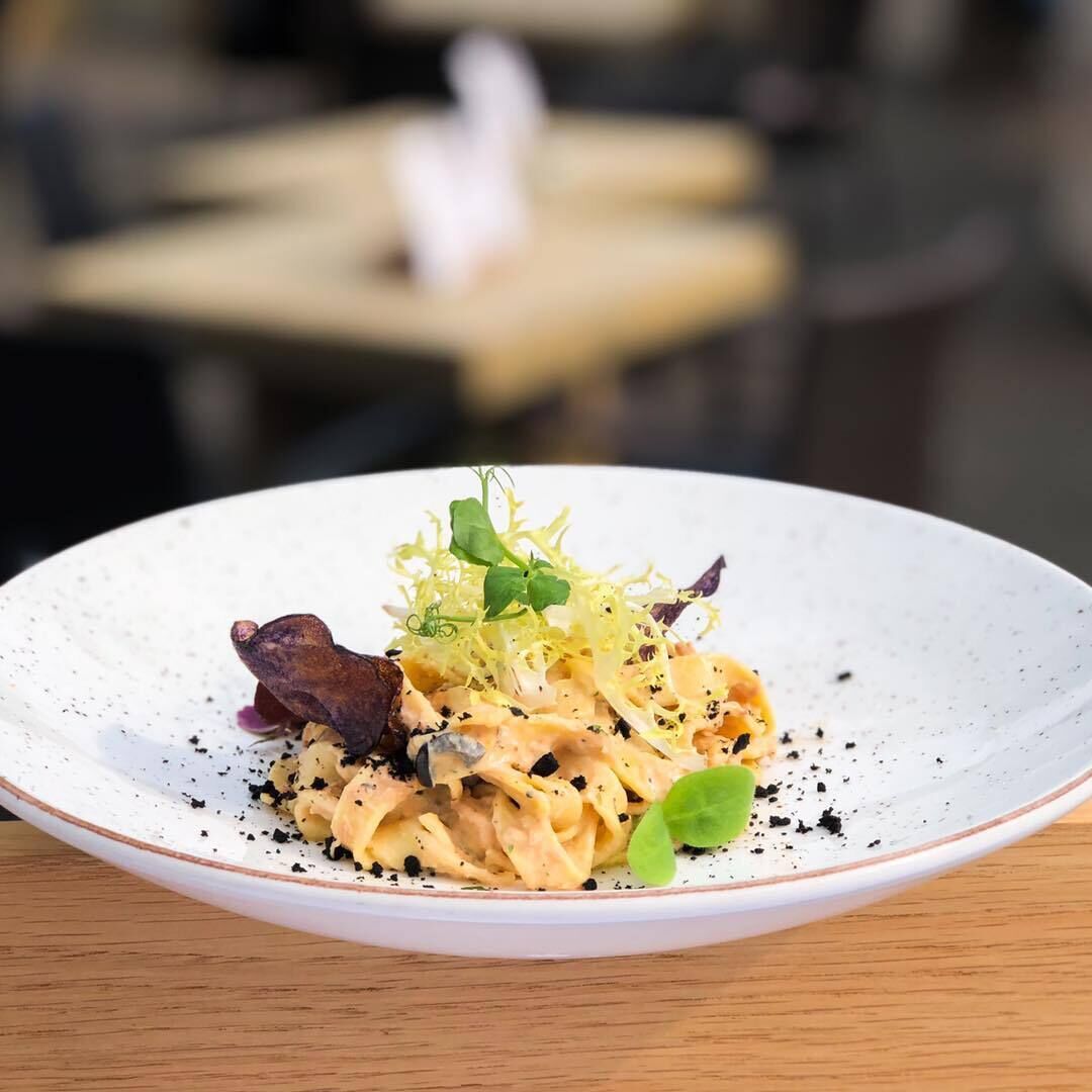Un plato de comida con pasta, vegetales verdes y un trozo de carne, servido en un plato blanco con diseño moteado.