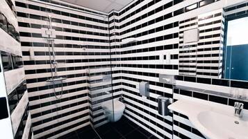 A modern bathroom with black and white striped tiles, a glass shower enclosure, a white sink, and a toilet.