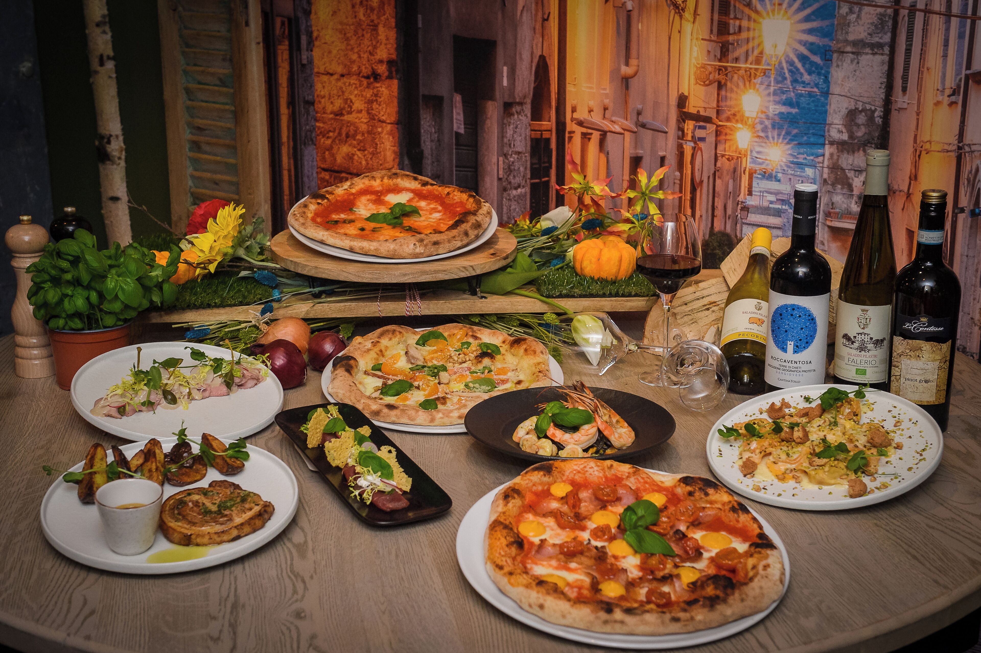 A variety of pizzas and wine bottles on a wooden table.