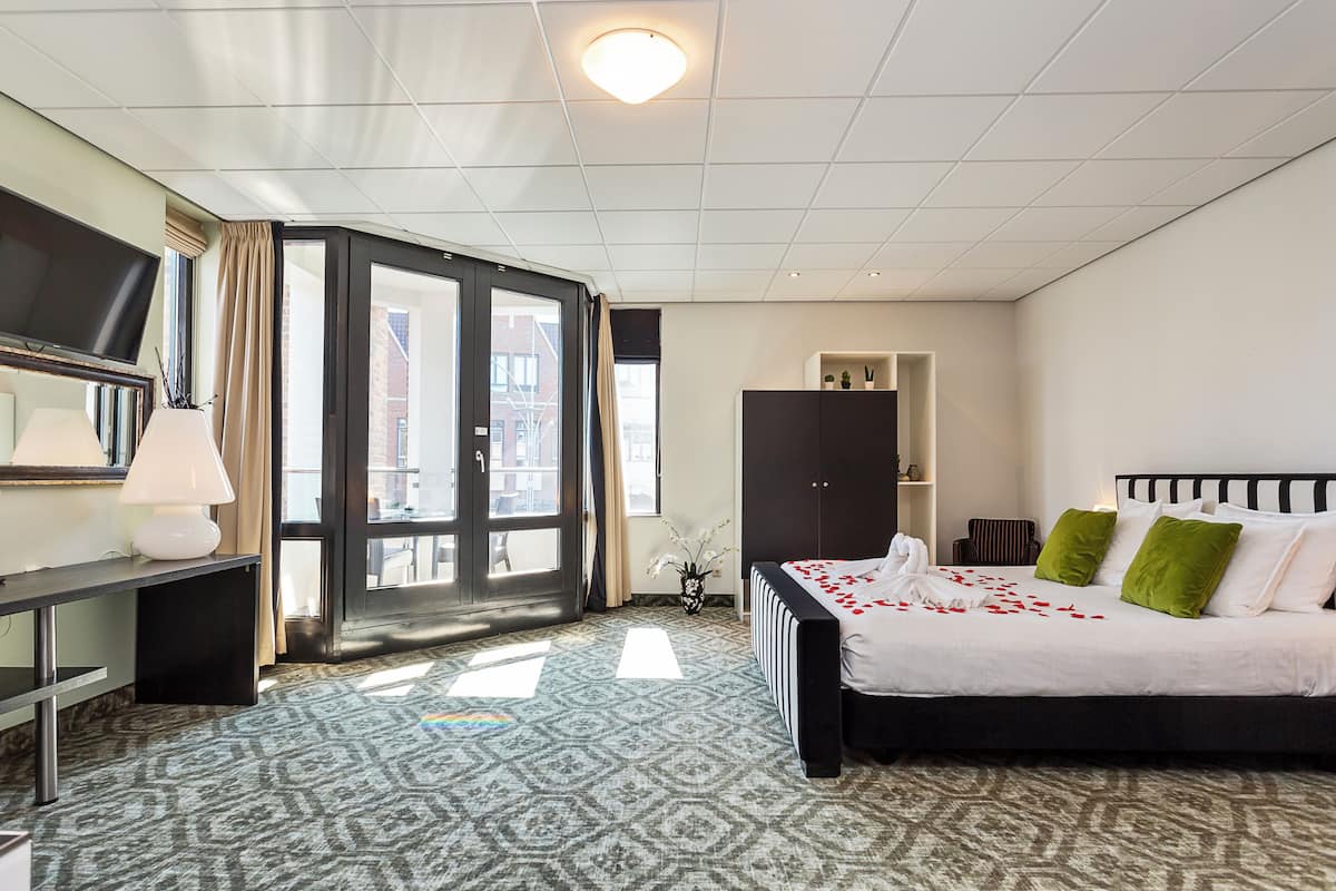 A hotel room with a bed, a desk, a TV, and a large window.