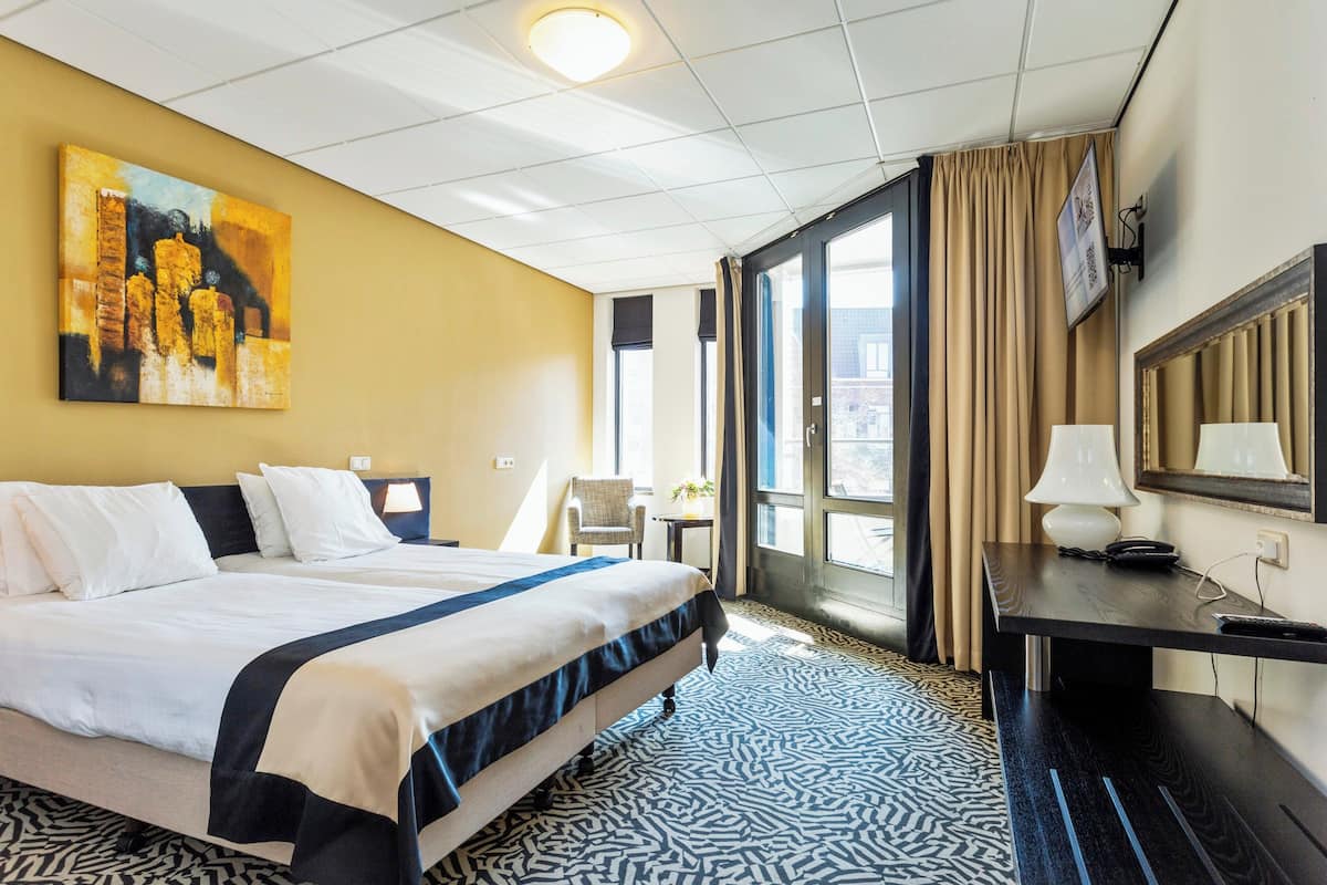 A hotel room with a bed, a desk, a chair, a TV, and a painting on the wall.