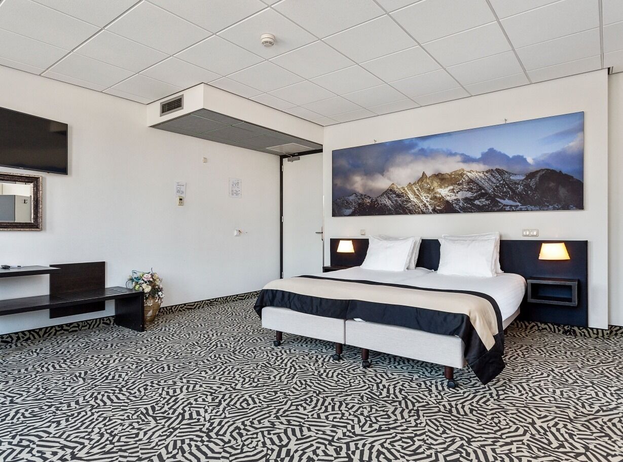 Una habitación de hotel moderna con una cama grande, un escritorio y un televisor montado.