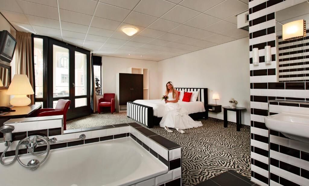 Ein Hotelzimmer mit einem großen Bett, einer separaten Sitzecke mit einem Sessel, einem kleinen Tisch, einer großzügigen Badewanne und einem am Wand montierten Waschbecken.