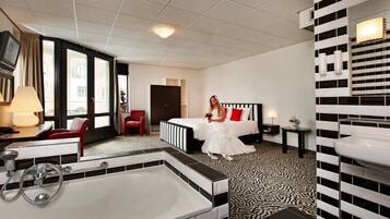 Ein Hotelzimmer mit einem großen Bett, einer separaten Sitzecke mit einem Sessel, einem kleinen Tisch, einer großzügigen Badewanne und einem am Wand montierten Waschbecken.