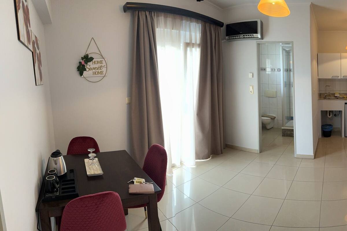 Habitación de hotel con cama, televisor, escritorio con silla, zona de comedor con mesa y sillas, y baño.