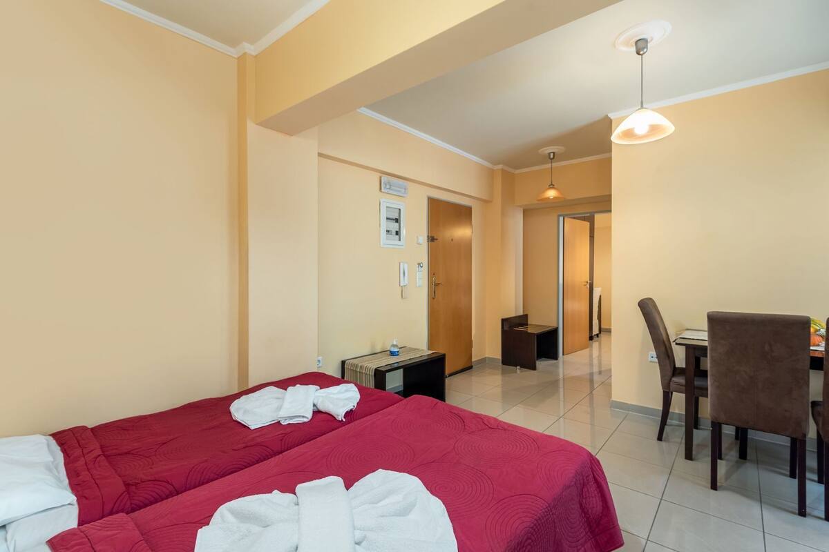Habitación de hotel con dos camas, un escritorio, una silla, una mesa de comedor y un pasillo que conduce a otra habitación.