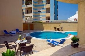 A pool area with lounge chairs, a table, and a view of a building. - Comfort Hotel (Rhodes)