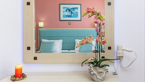Een slaapkamer met een bed, nachtkastje, spiegel, lamp, vaas met bloemen en een haardroger.