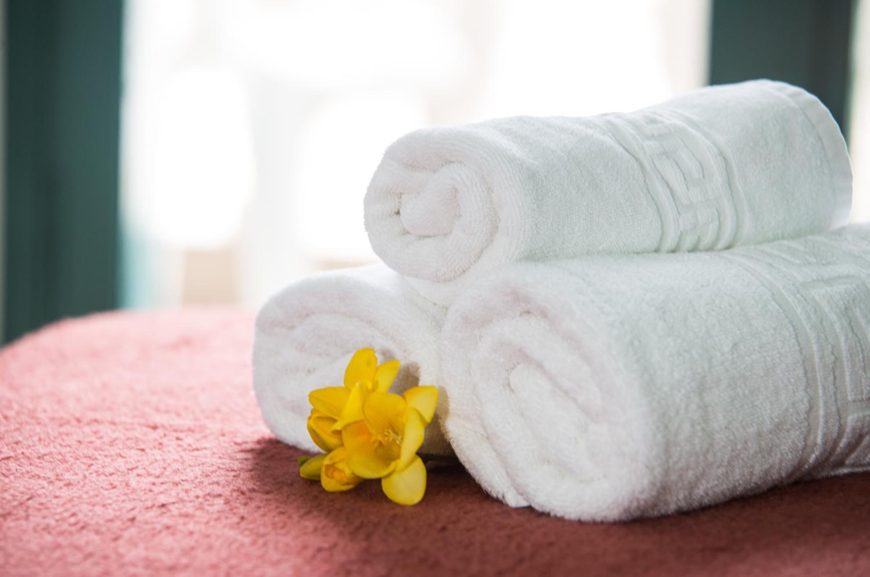 A stack of white towels on a pink surface with a yellow flower beside them.