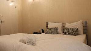 A neatly made bed with two patterned pillows, a rolled towel, and a bedside table with a lamp and a cup. - Avenue Inn (London)