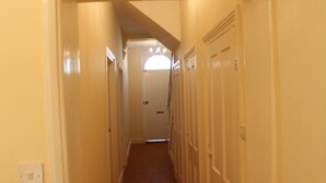 A narrow hallway with doors on both sides leading to a room with a window and a chandelier. - Avenue Inn (London)