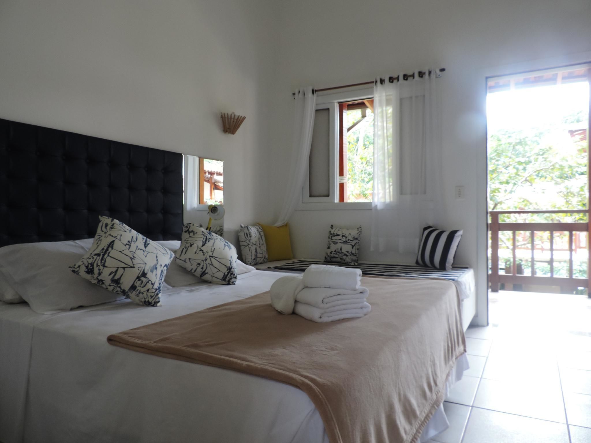 Quarto de hotel com duas camas, uma janela grande com cortinas e vista para áreas verdes lá fora.