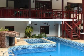 A two-story building with a swimming pool, wooden balcony railings, and a staircase.