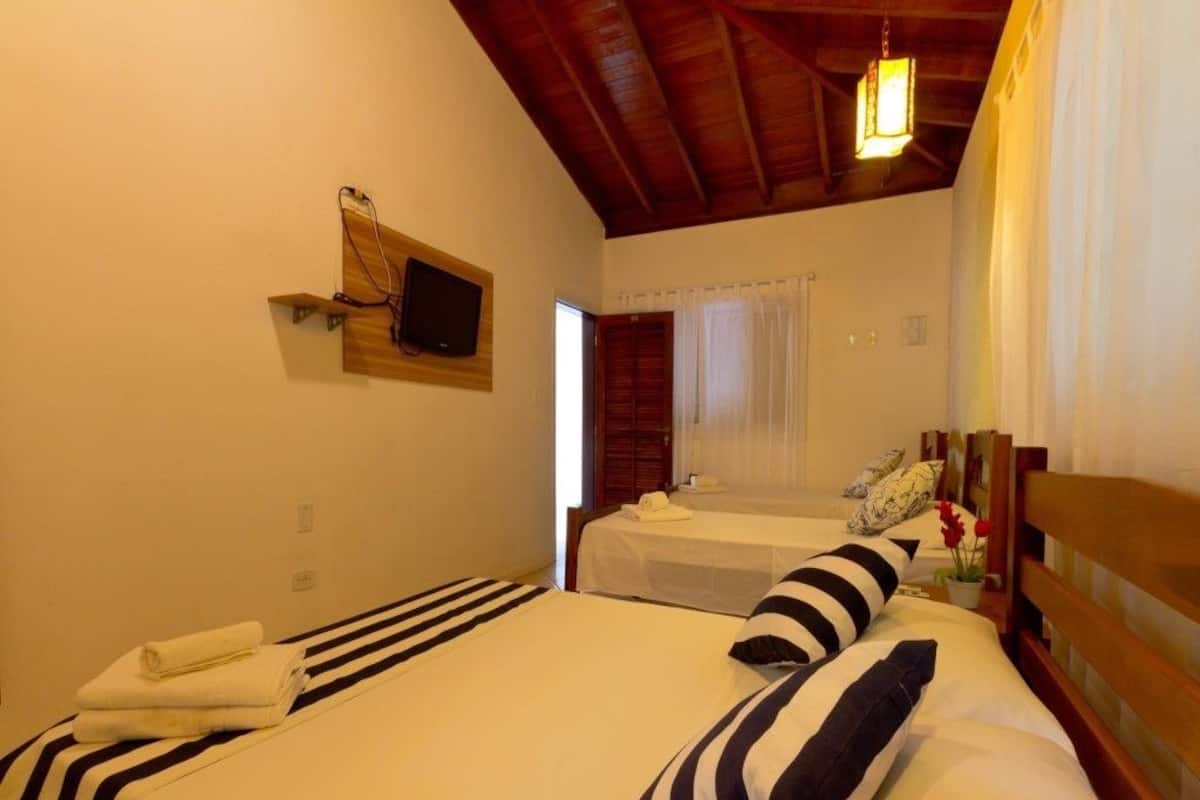 Ein Hotelzimmer mit zwei Betten, einem an der Wand montierten Fernseher und einer Holzbalkendecke.
