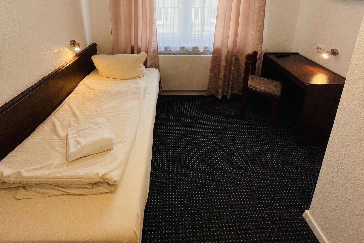 Une chambre d’hôtel avec un lit, un bureau, une chaise et une fenêtre avec des rideaux.