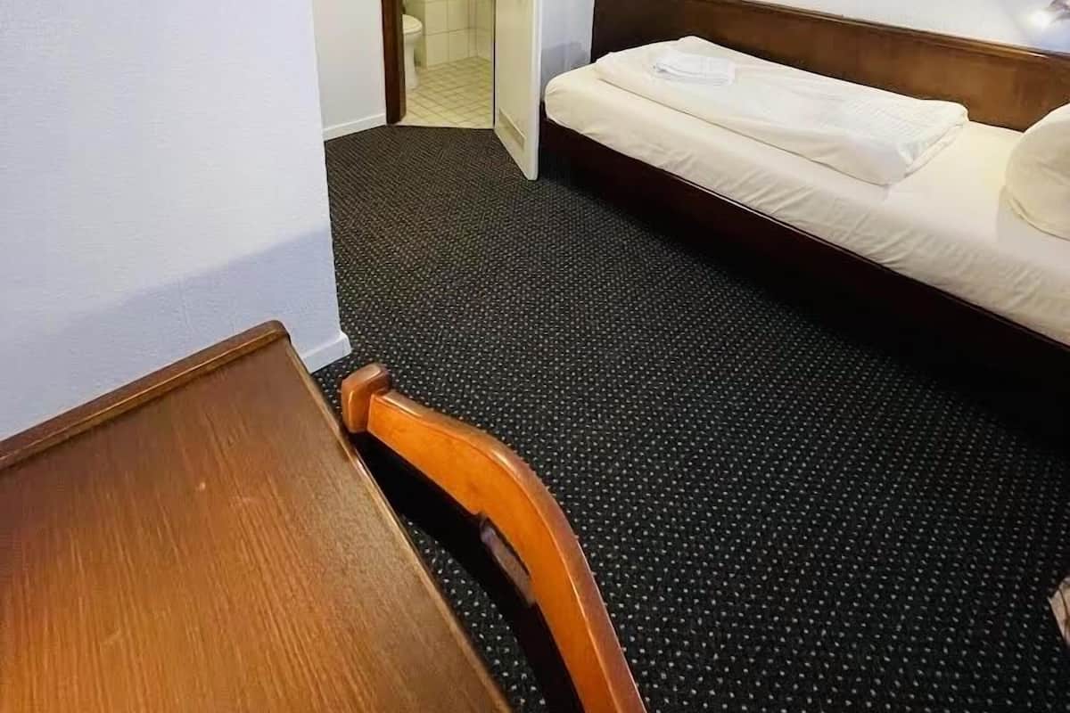Une chambre d’hôtel avec un lit, une chaise, un bureau, un miroir et une porte de salle de bain.