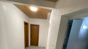 A hallway with a carpeted floor, white walls, and a wooden ceiling. There is a door labeled '14' and an exit sign on the right wall. - Brunnen Hotel (Essen)