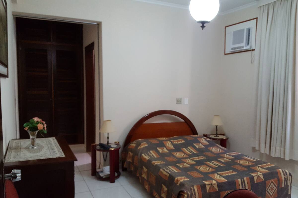 Une chambre à coucher comprenant un lit, des tables de chevet, une commode, une lampe, une fenêtre et une porte.