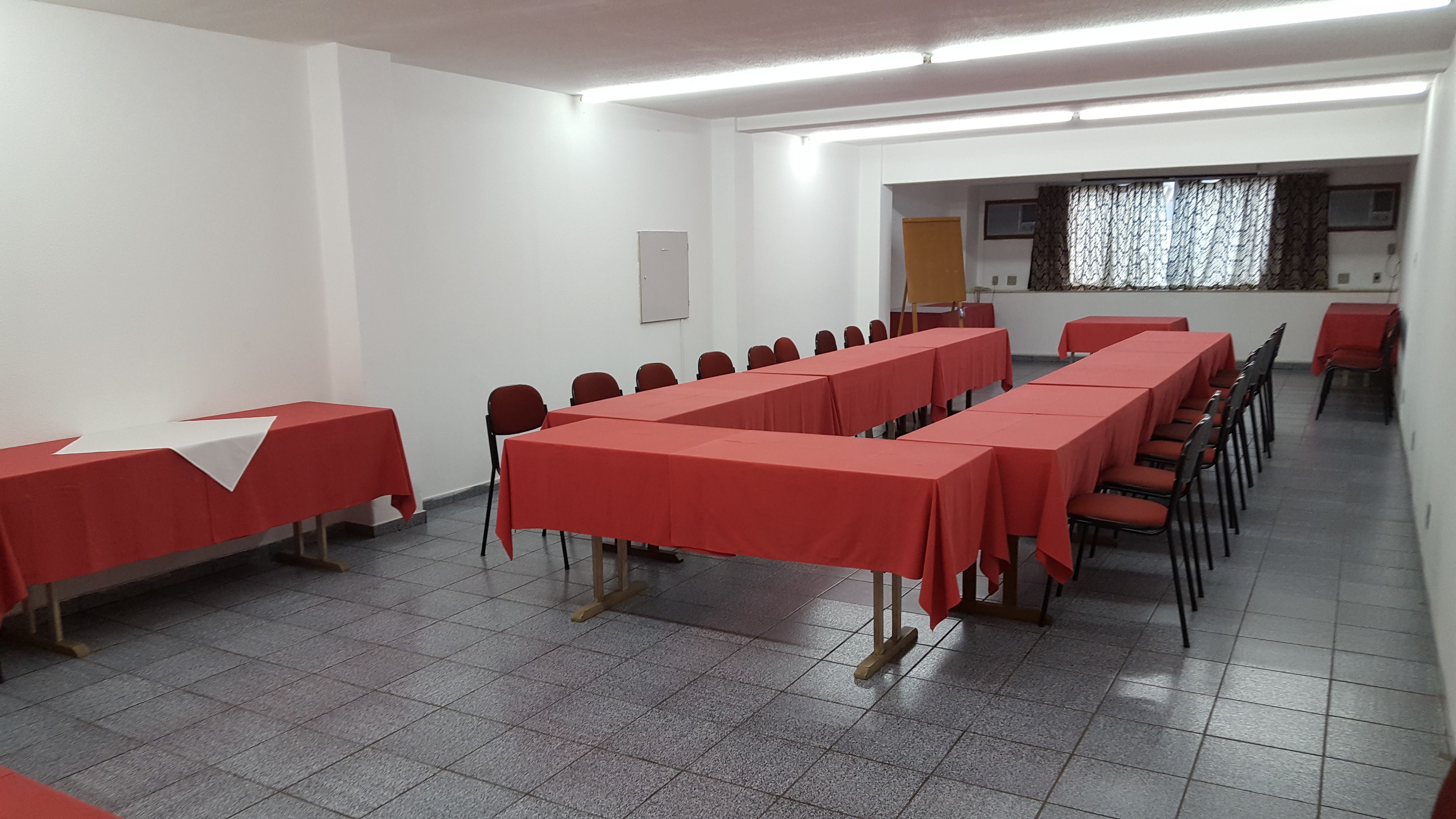 A conference room with long tables covered in red tablecloths, arranged in rows.