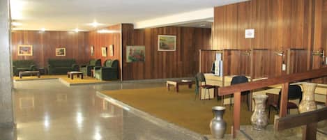 A lobby with wooden paneling, a reception desk, several chairs, a staircase, and a vase on the floor.