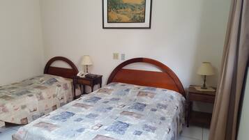 Una habitación con dos camas, cada una con cabecero de madera, una mesita de noche con lámpara y un cuadro en la pared.