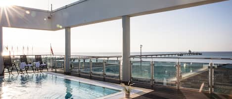 A rooftop pool with a view of the sea and a pier in the distance.