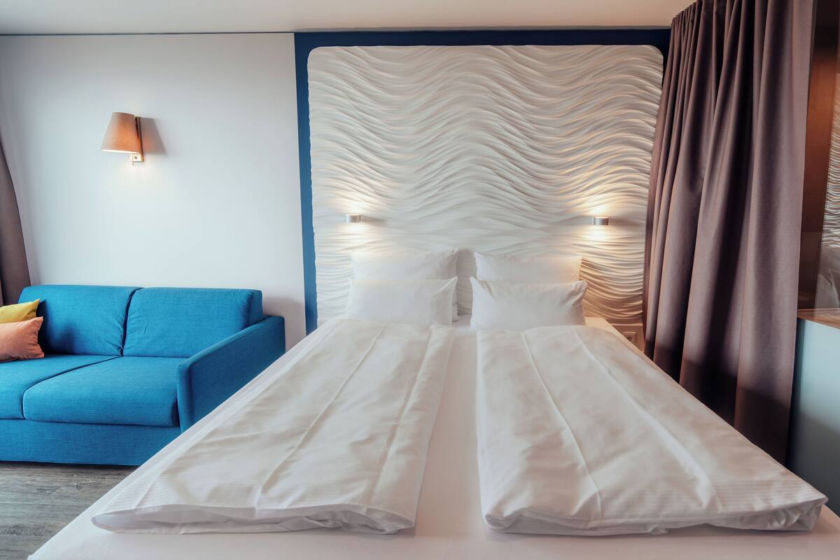A modern hotel room with a large bed, a blue sofa, and a textured wall.