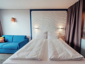 A modern hotel room with a large bed, a blue sofa, and a textured wall.