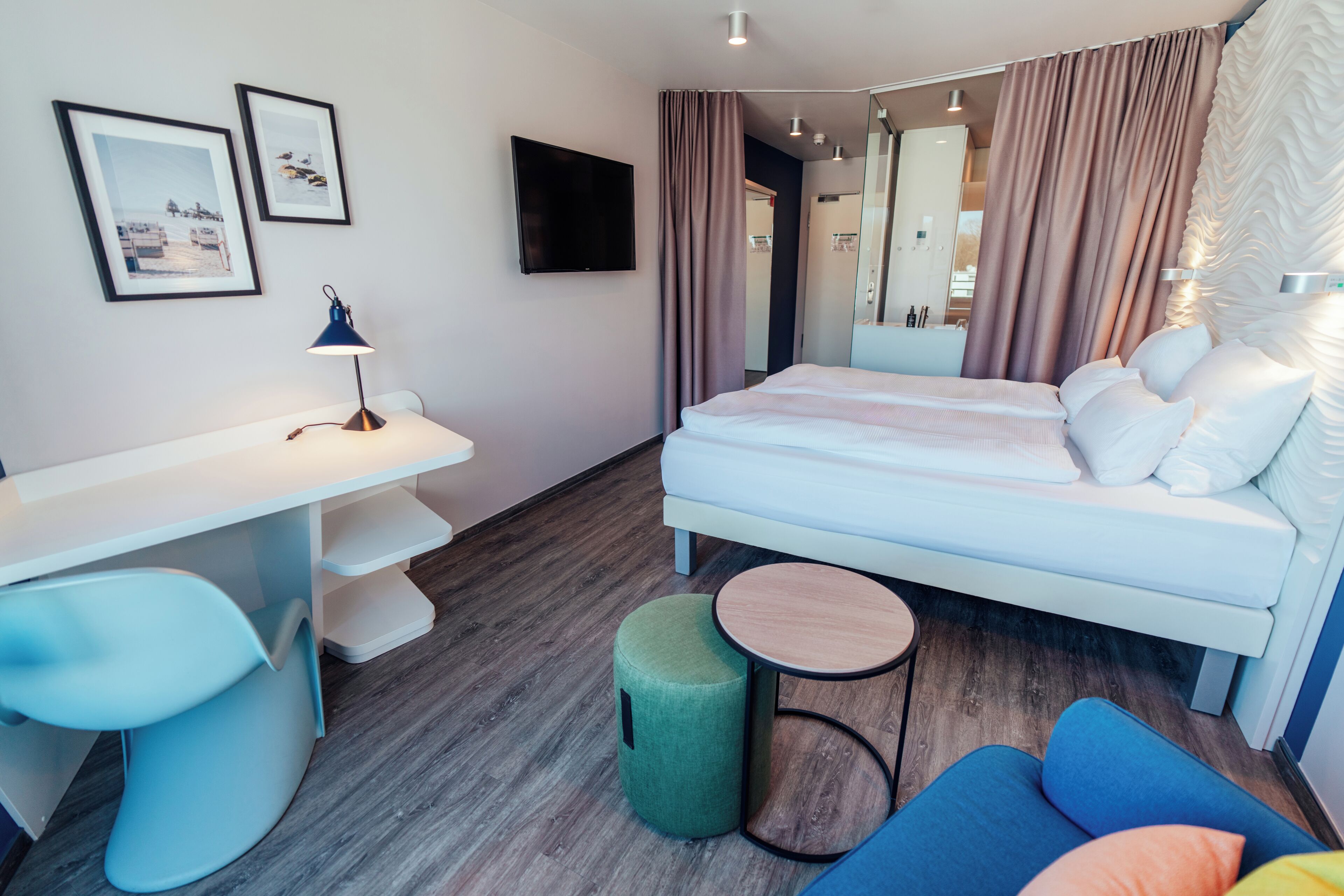 A modern hotel room with a bed, a desk, a chair, a round table, and a mirror.