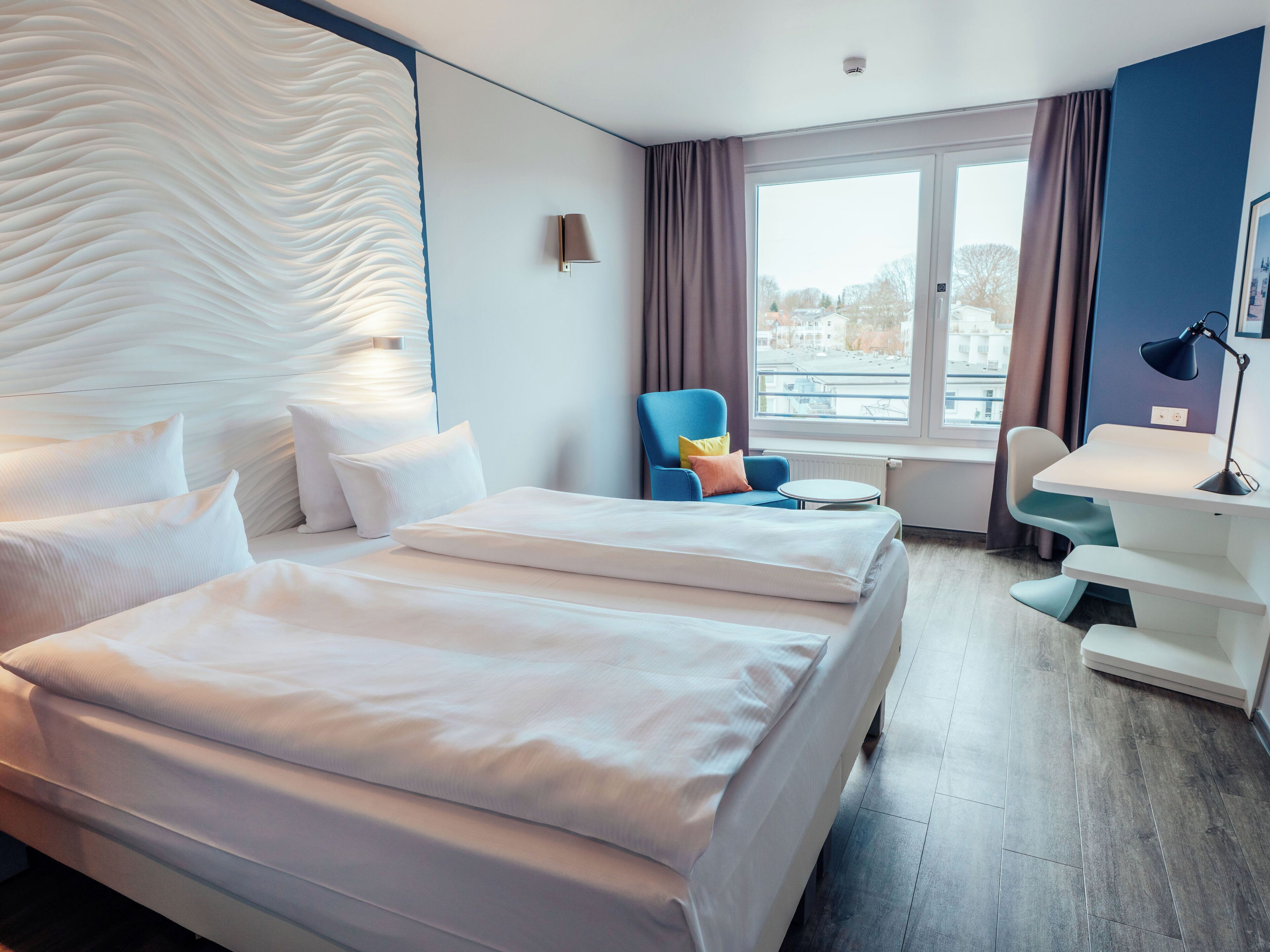 Hotellihuone, jossa on sänky, työpöytä, tuoli ja näkymä kaupunkiin.