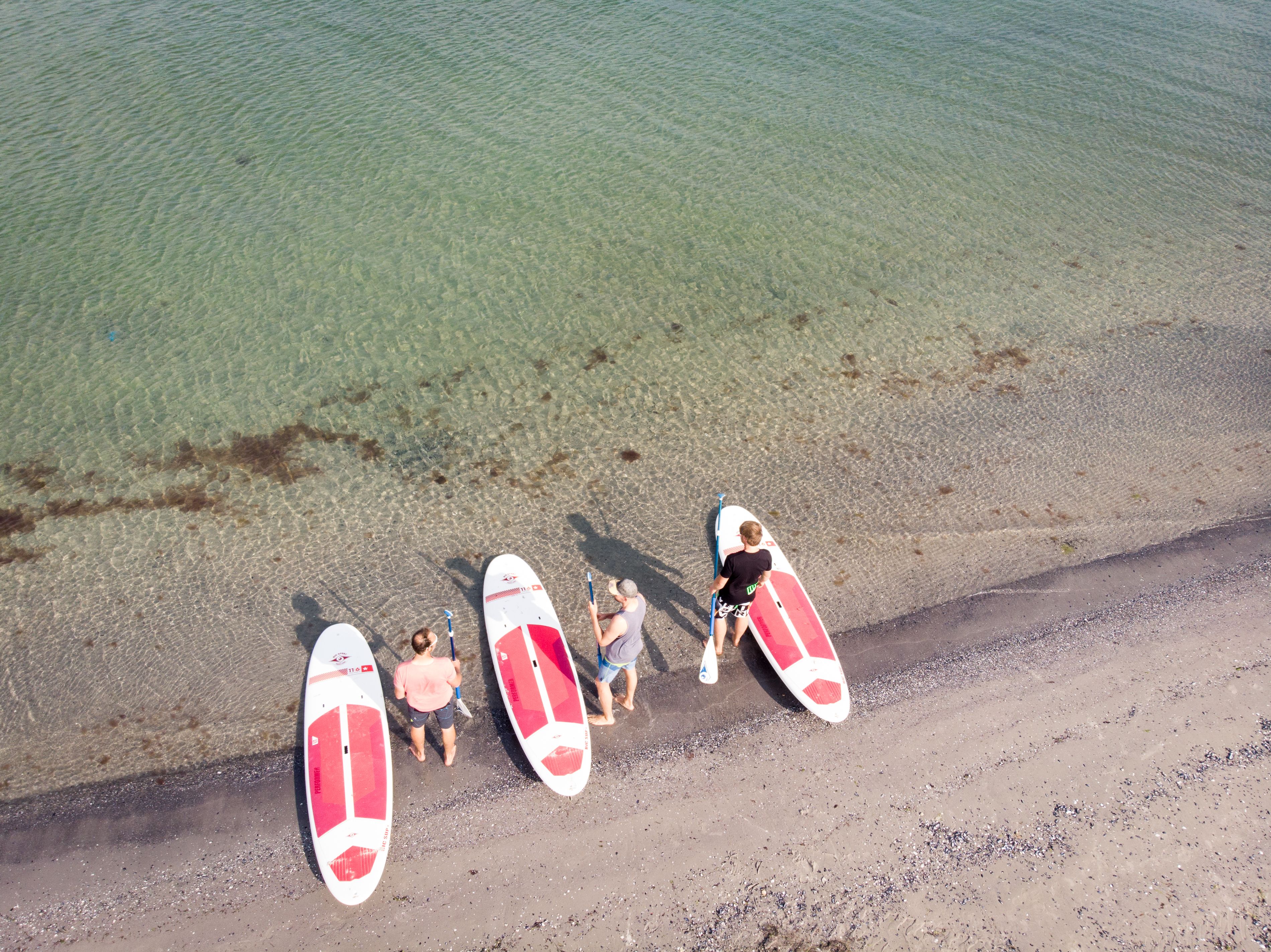 An aerial view of a beach with clear water and several surfboards lined up on the shore.
