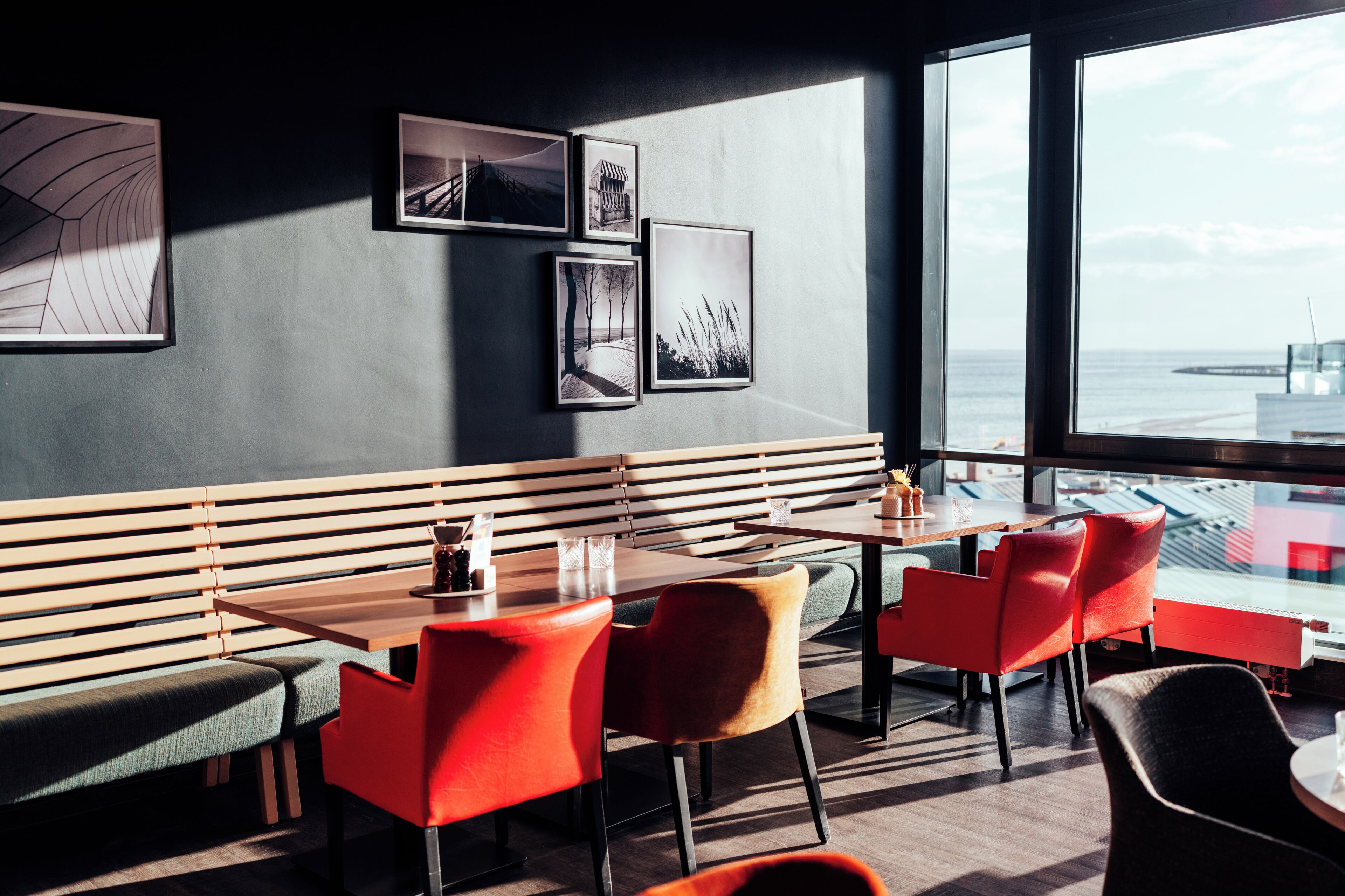 A restaurant with wooden benches and red chairs, a table with glasses, and framed pictures on the wall.